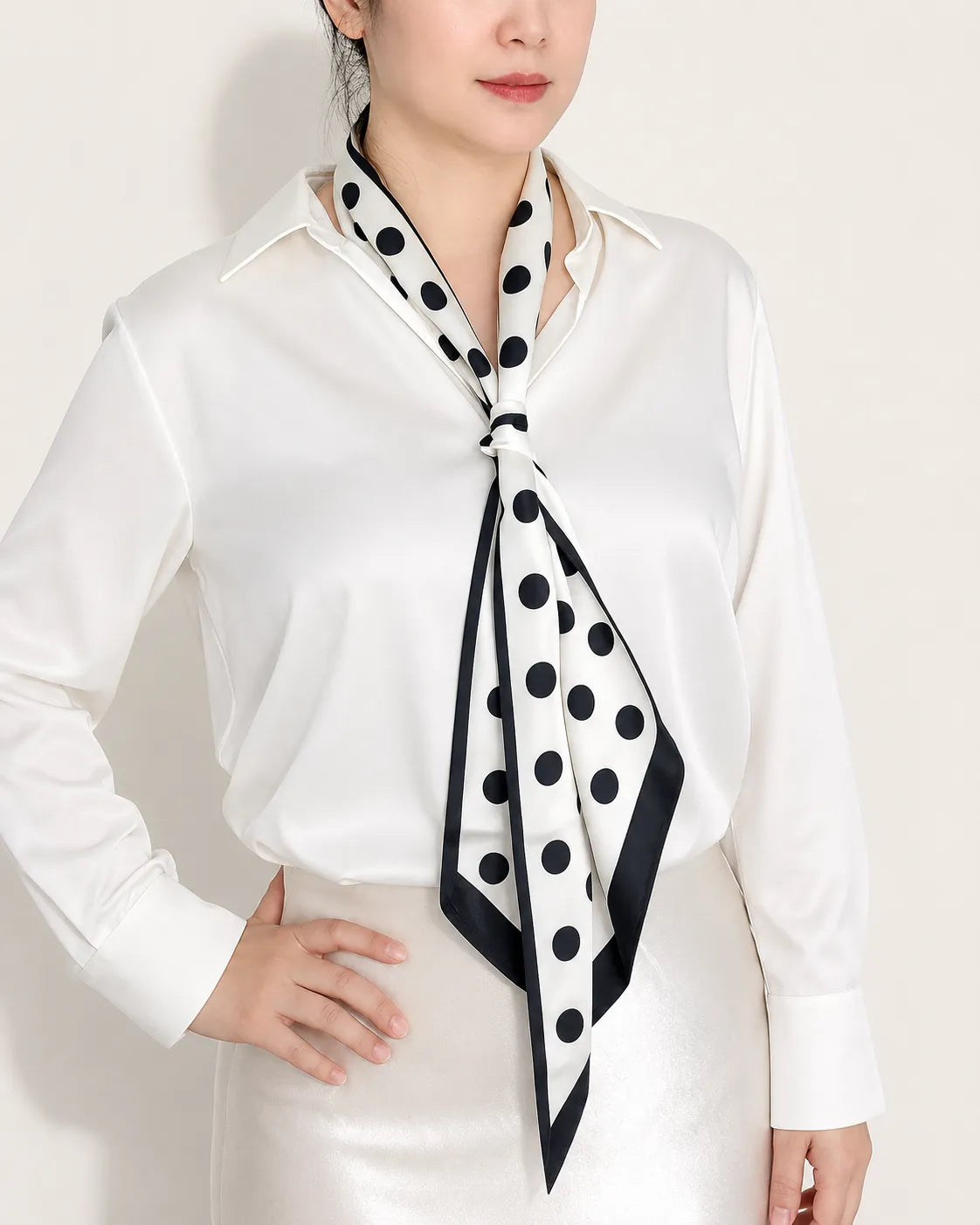 A professional front view of a woman wearing a white button-down shirt, styled with a white and black polka dot satin skinny scarf tied elegantly around her neck.