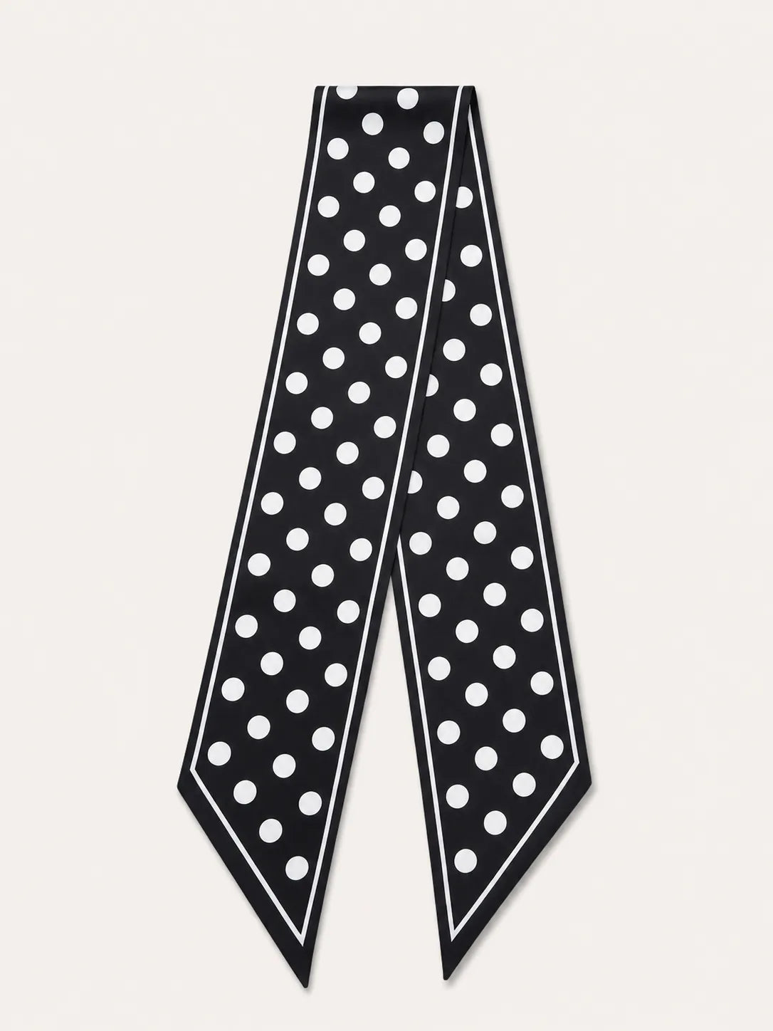 A minimalist product flat lay of a black satin skinny scarf with a classic white polka dot pattern against a clean, light off-white background.