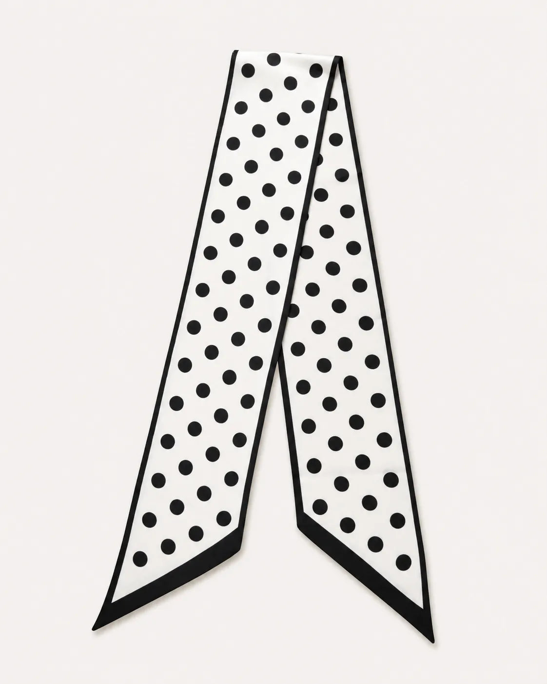 A minimalist product flat lay of a white satin skinny scarf with a classic black polka dot pattern against a clean, light off-white background.